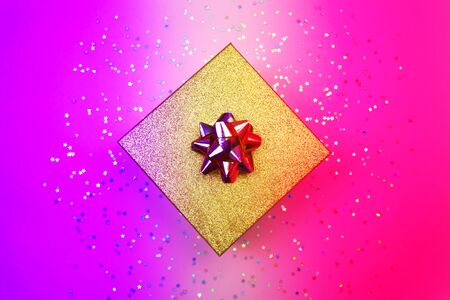 Golden gift box with ribbon and rainbow holographic stars confetti. Minimal flat lay in led neon light background. Top view festive banner, social media. Trendy blue violet and magenta modern gradientの写真素材