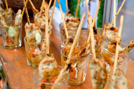 Snacks set on wooden table. Street food tasting appetizer, degustation. Meat, fish, chicken skewers with dressing in glass shots. Fresh cooking festival, market, catering service. Selected focus macroの写真素材