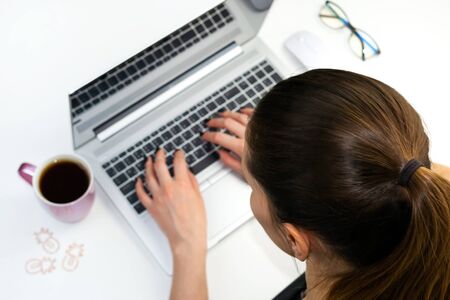 Freelancer young business woman working on laptop. Flat Lay, top view. Remote distant home office, stay home isolated concept. Computer, pink cup of tea or coffee, glasses. Lockdown quarantine indoor.の写真素材