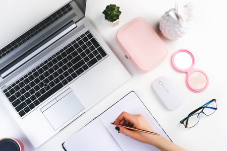 Woman's hand writes in a notebook and working on laptop.