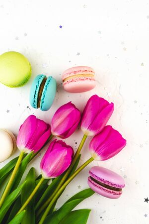 Tulips flowers and macaroons on a bright grey, white concrete texture background. Flat Lay. Spring floral pastel concept top with confetti stars. Holiday, birthday French delicious dessertの写真素材