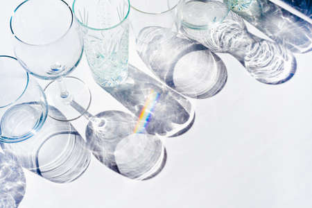 Many empty crystal glasses in a row on white table background. Transparent party beverage cups silhouette on sunlight, hard shadow. Trendy flat lay monochrome pattern with copy space. Art conceptの写真素材