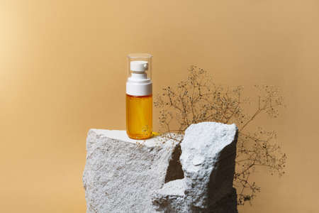 Serum or essential oil osmetic in bottle with pump on grey concrete stone podium, dried flowers on beige background. Trendy natural organic spa concept. Minimal scene presentation mockup, copy spaceの写真素材