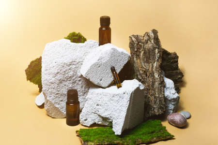 Three essential oil bottles on stone, moss, wood gardening podium on bright beige background. Beauty aroma cosmetic set, organic medical skincare spa treatment. Trendy healthy packaging conceptの写真素材