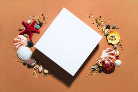 White close square gift box mockup template top view with copy space. Layout package clipart. Tropical seashells, sand and stones decor. Summer modern concept flat lay on brown orange backgroundの写真素材