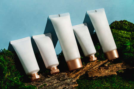 Many cosmetics tubes on green moss and bark forest background. Blank label package for branding mockup. Natural spa beauty product closeup. Cream, serum, mask, moisturizer, lotion skincare clipartの写真素材