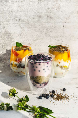 Still life of sliced fruit desserts in glass jar. Organic sweet chia seed superfood pudding. Fresh dairy sweet blueberries and peach fruit breakfast on bright gray concrete background. Vegan foodの写真素材