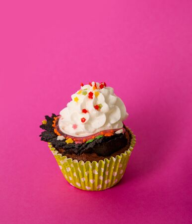 Cupcake with whipped cream and heart-shaped decor on a pink backgroundの写真素材