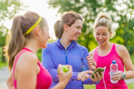 Group of happy active girls preparing for a run in nature by choosing music on smart phoneの写真素材