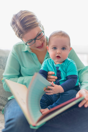 Adorable toddler flipping the pages of a picture book on his moms lap