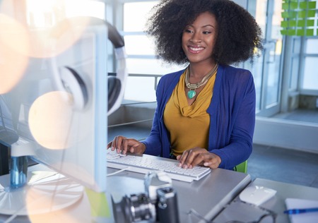 Friendly african american casual business woman working at a desktop computer in a modern withe officeの写真素材