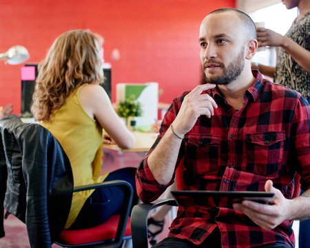 Casual portrait of a business man using technology in a bright and sunny startup with the team in the backgroundの写真素材
