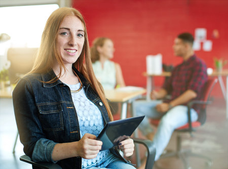 Casual portrait of a business woman using technology in a bright and sunny startup with the team in...
