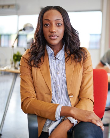 Casual portrait of an african american business woman using technology in a bright and sunny startup with windows in the backgroundの写真素材