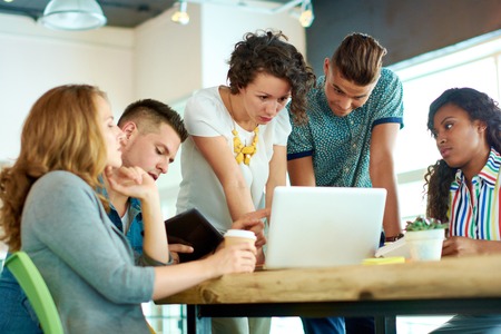 Group of young casual employees discussing a project while researching ideas in a digital touchscreen device and a laptop.の写真素材