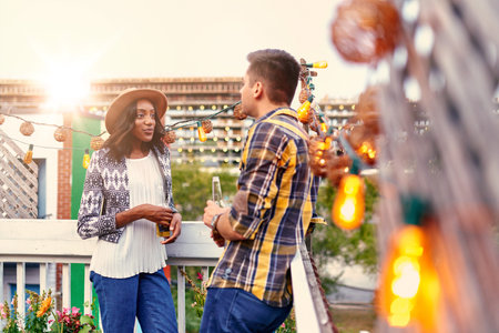 Two young casual friends having a casual conversation at an urban celebration with a cityscape view...