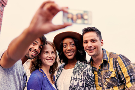 Four young casual friends having fun taking pictures at an urban celebration with a cityscape view in the eveningの写真素材