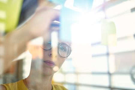 Team of young casual business people collaborating on an creative planning project using a blue and yellow sticky notes in a bright modern office space. Serie with light flares and glass reflectionsの写真素材