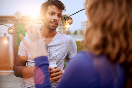 Two young casual friends having a casual conversation at an urban celebration with a cityscape view in the eveningの写真素材