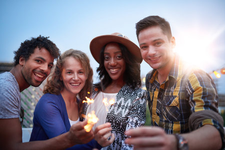 Four young casual friends having fun with sparkling lights at an urban celebration with a cityscape...
