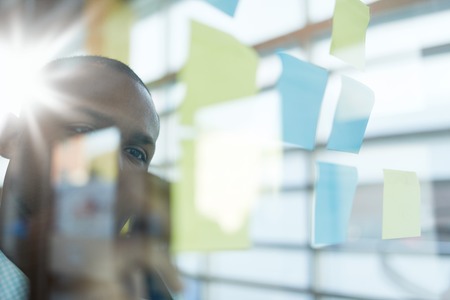 Team of young casual business people collaborating on an creative planning project using a blue and yellow sticky notes in a bright modern office space. Serie with light flares and glass reflectionsの写真素材