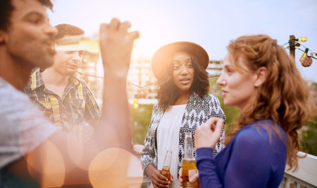 Four young casual friends having fun at an urban party and having a drink with cityscape view