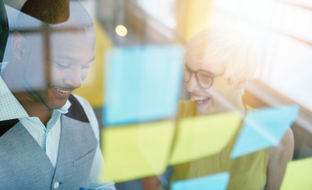 Team of young casual business people collaborating on an creative planning project using a blue and yellow sticky notes in a bright modern office space. Serie with light flares and glass reflectionsの写真素材