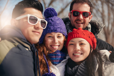 Group of millenial young adult friends photographing each other with a smartphone in a snow filled parkの写真素材