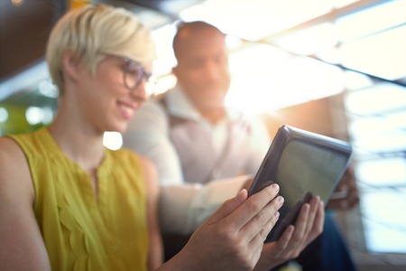 Team of young casual business people collaborating on an online project using a digital touchpad tablet computer in a bright modern office space. Serie with light flaresの写真素材
