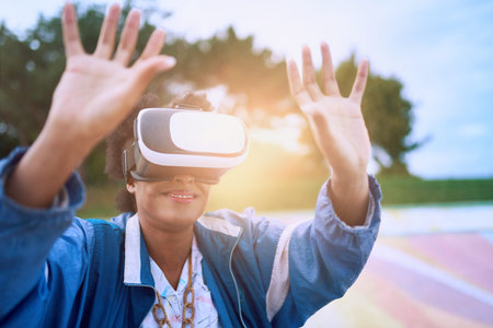 Smiley young African American woman alienated by new technology wearing VR goggles in a skate park...