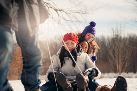 Group of millenial young adult friends enjoying wintertime and sledding in a snow filled parkの写真素材