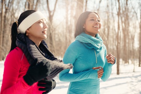 Diverse duo of millenial young adult friends take a break while training for cross-country running in the wintertime in a snow-filled parkの写真素材