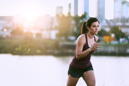 Portrait of active millenial woman jogging at dusk with an urban cityscape and sunset in the backgroundの写真素材
