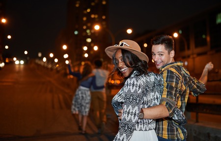 Multi-ethnic millenial group of friends taking a selfie photo with mobile phone on rooftop terrasse using flash at night timeの写真素材