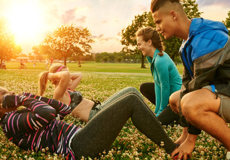 Diverse group of millenials during fitness class doing sit-ups at sunset in nature parkの写真素材