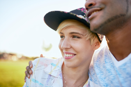 Mixed race couple of millennials in a grass field cuddling and showing affection togetherの写真素材