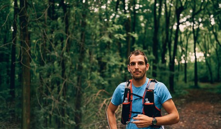 Fit male jogger rests during day jogging for cross country forest trail race in a nature park.の写真素材