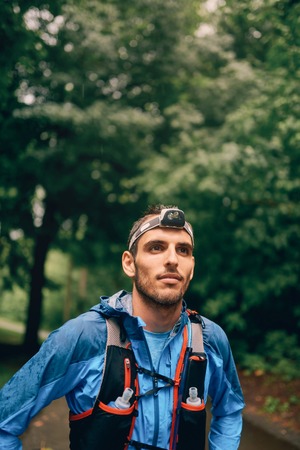 Fit male jogger with a headlamp rests during training for cross country trail race in nature park.の写真素材