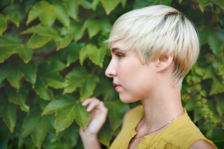 Beautiful short haired platinum blond woman standing against an ivy fence backdropの写真素材