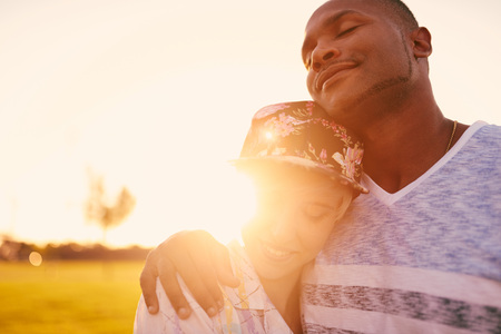 Mixed race couple of millennials in a grass field cuddling and showing affection togetherの写真素材