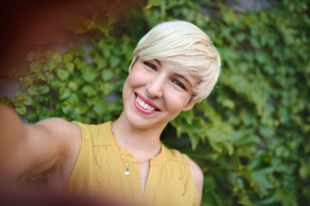 Attractive white woman taking a selfie against an ivy fence backdrop