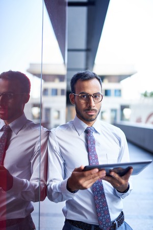 Millenial businessman leaning confidently on a dark glass wall with cityscape backgroundの写真素材