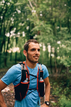 Fit male jogger rests during day jogging for cross country forest trail race in a nature park.の写真素材