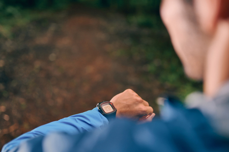 Fit male jogger day using a smartwatch during cross country forest trail race in a nature park.の写真素材