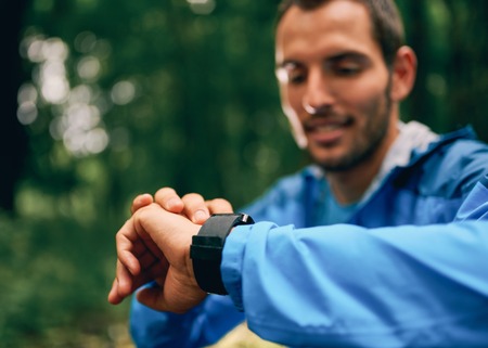 Fit male jogger day using a smartwatch during cross country forest trail race in a nature park.の写真素材