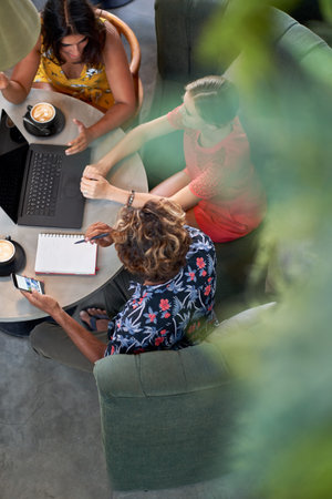 Candid lifestyle shot of three diverse millennial colleagues planning over coffee with laptop...