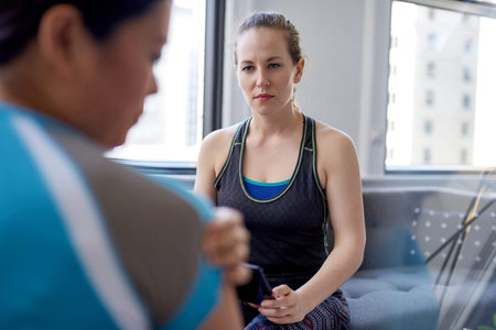 Caucasian woman physiotherapist talking to a mid-adult chinese female patient and taking notes on a...