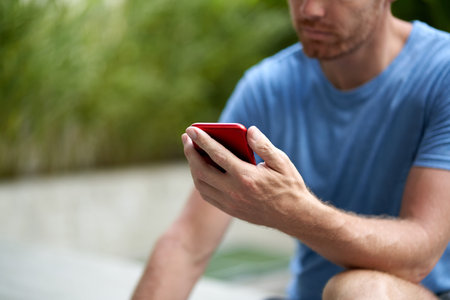 Candid lifestyle closeup shot of handsome with beard man sitting holding cellphone reading emails in...