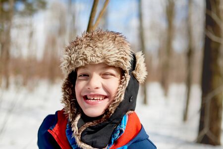 Portrait of a smiling boy enjoying playing in fresh snow during wintertime and wearing a fur trimmed hatの写真素材