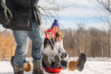 Group of friends enjoying pulling a sled in the snow in winter